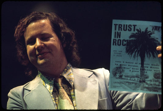 “Blue” Gene Tyranny with Trust in Rock flyer designed by Phil Harmonic. Photo: Pat Kelley