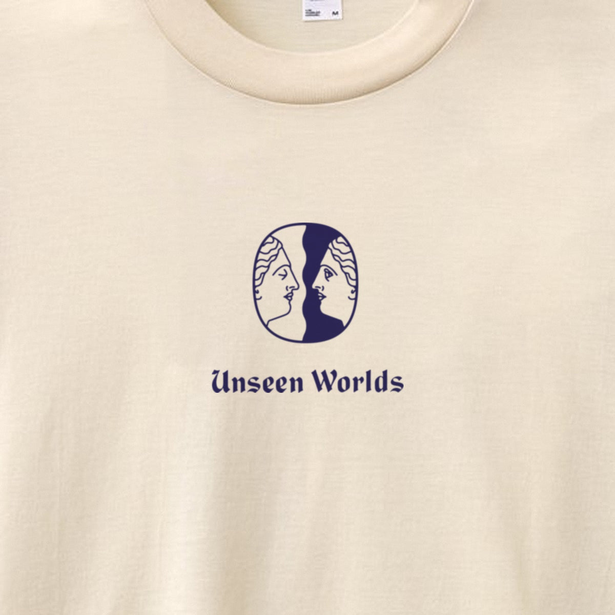 Close-up of the Unseen Worlds twin-face logo and wordmark printed in blue on the creme tee